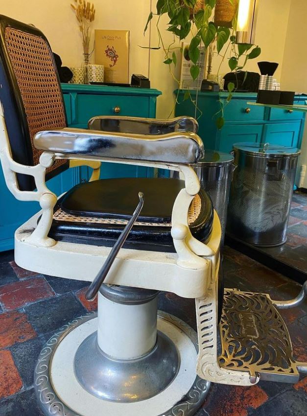 Een vintage witte kappersstoel met zwarte zitting voor de kasten in de salon