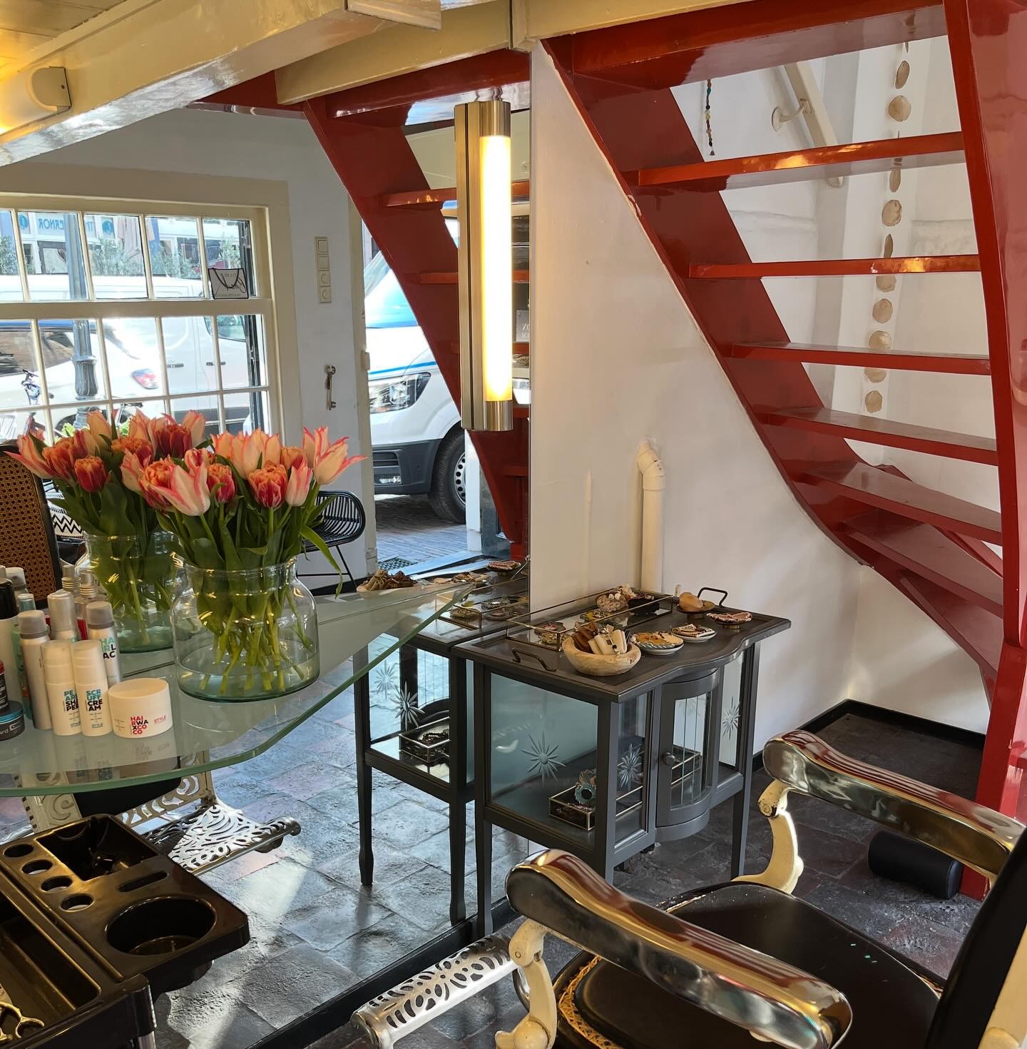 Roze en oranje tulpen op de glazen tafel naast een kappersstoel, met de rode trap op de achtergrond